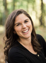 Smiling woman named Holly Tomlinson stands in a forest with trees in the background.