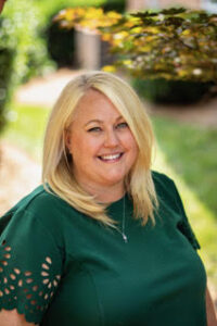 Rachel Cunningham, a woman with blonde hair, wearing a green shirt, smiles at the camera.